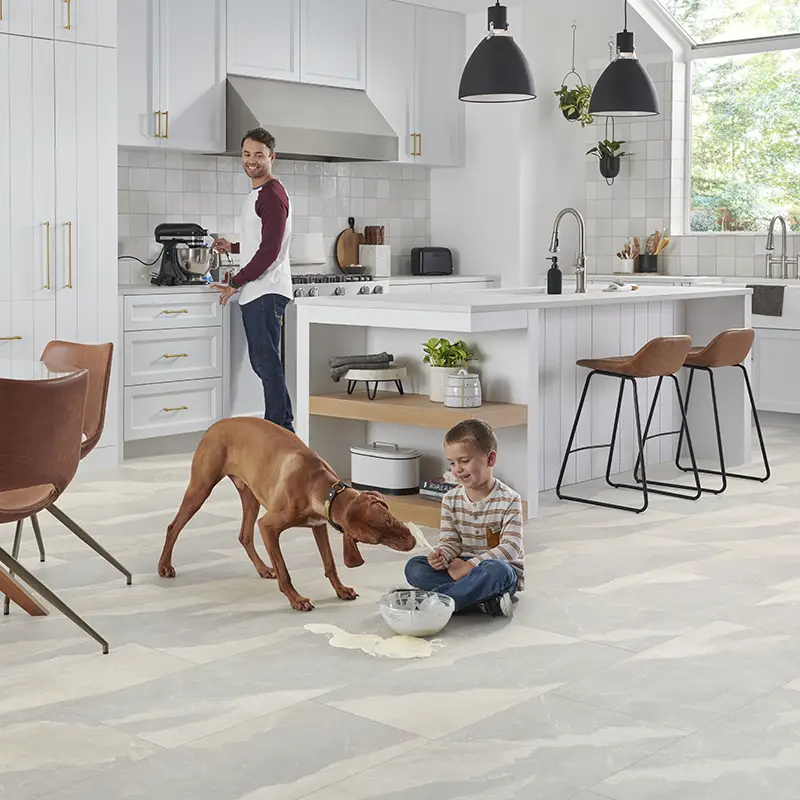 kid sitting on the luxury vinyl flooring in a kitchen letting a dog lick the beaters while dad stands at a stand mixer and watches