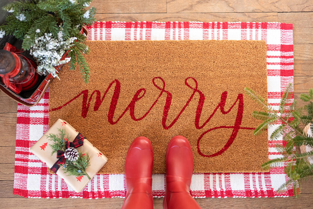 Merry doormat to help protect floors for Christmas, overhead view showing red boots on the mat 