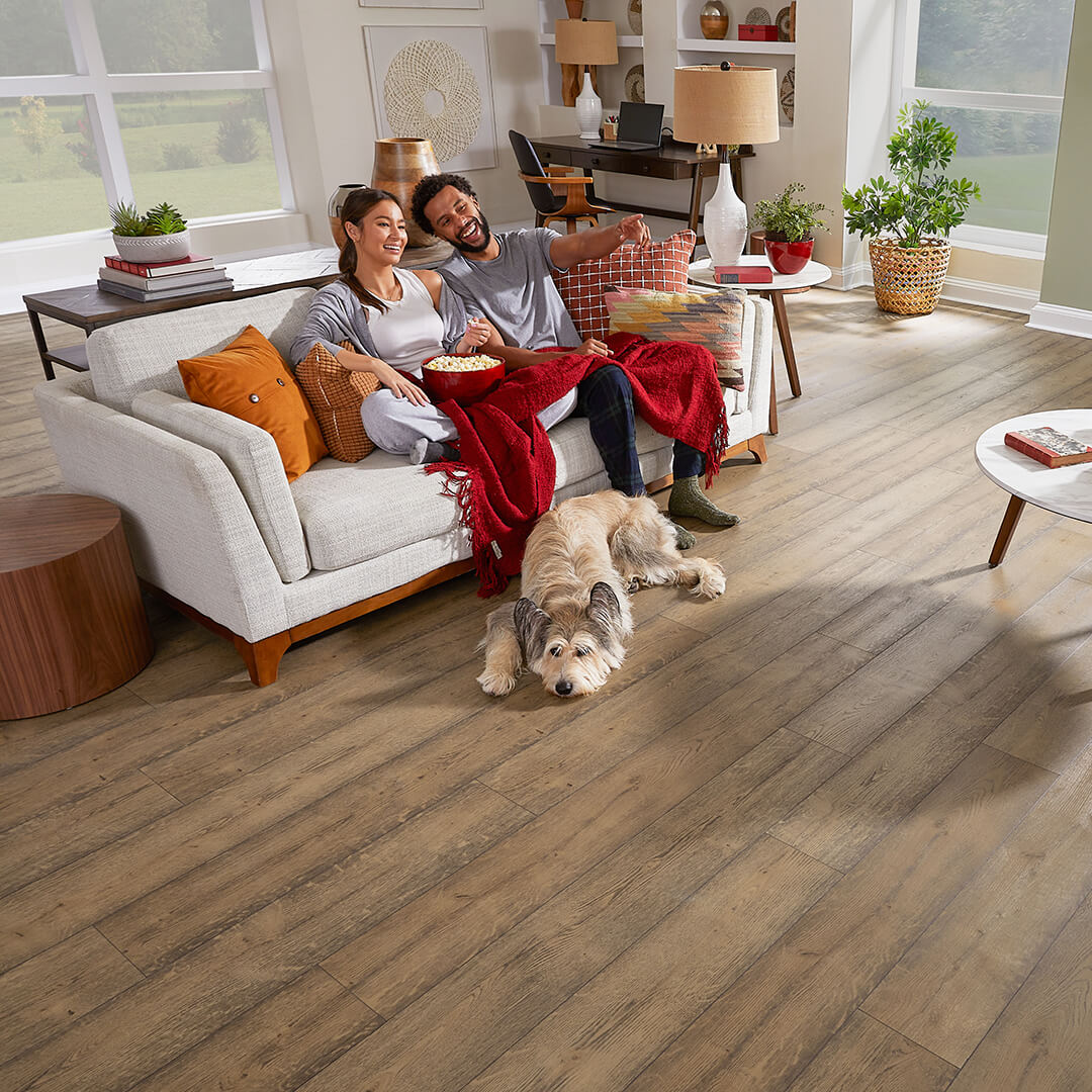 couple on a couch with dog at their feet, showing hardwood flooring